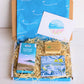 cornish coastal letterbox gift set with illustrated coaster, artisan chocolate and handcrafted soap